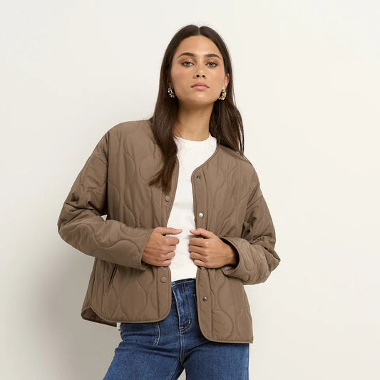 Woman wearing a brown jacket, white shirt, blue jeans, and white sneakers on a white background
