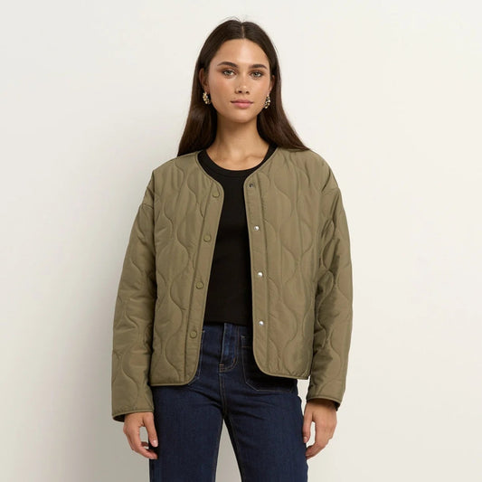 Woman wearing a green quilted jacket, black top, and blue jeans on a white background