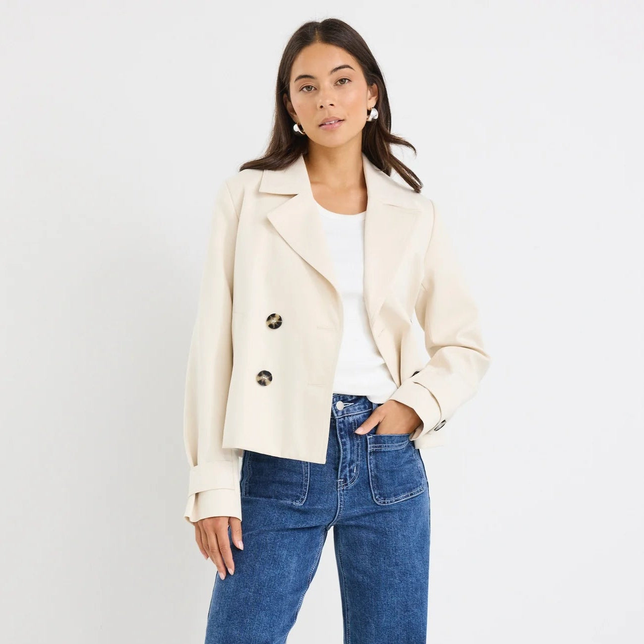 Woman wearing a cream blazer, white top, and blue jeans on a white background