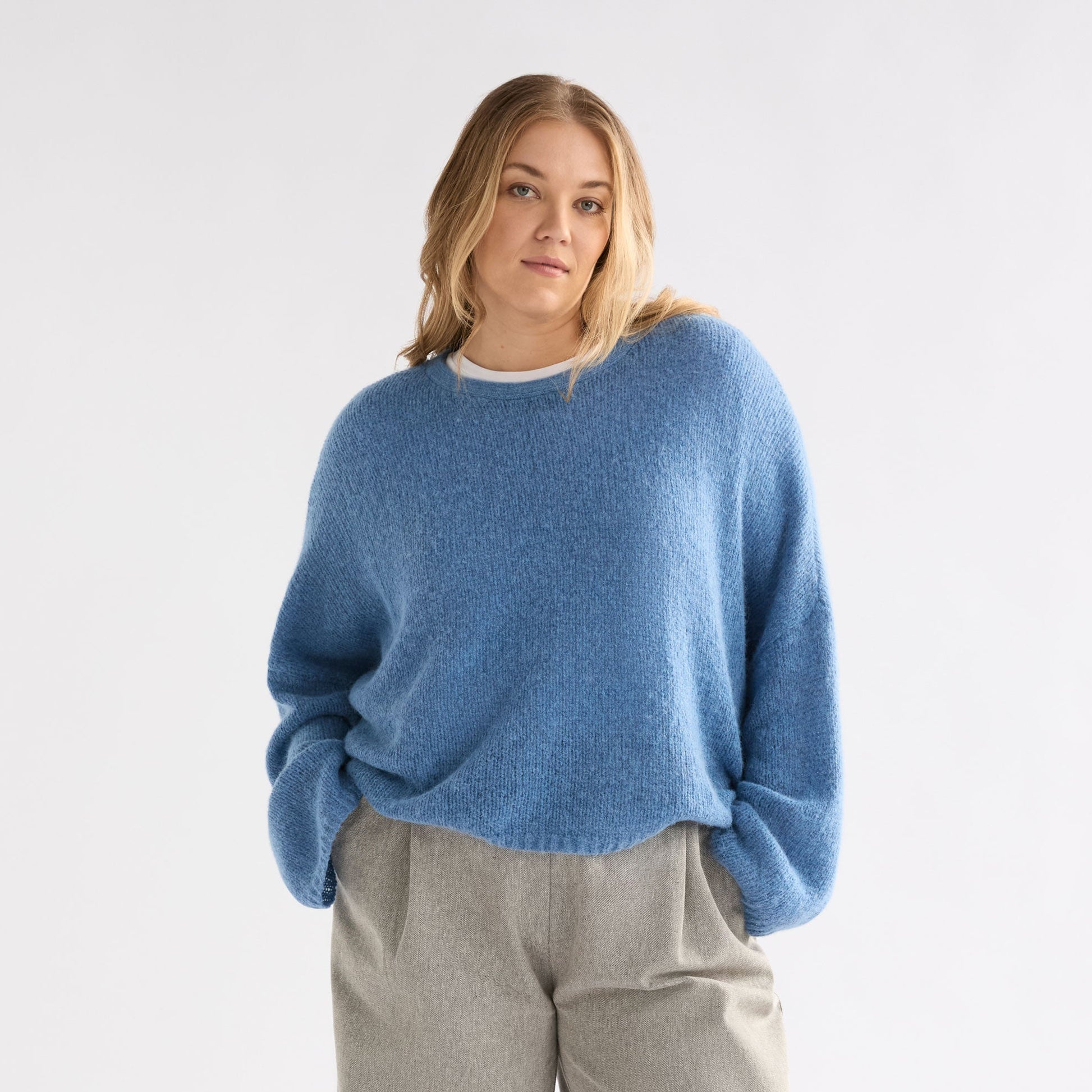 Person wearing a blue sweater and gray wide-leg pants on a white background