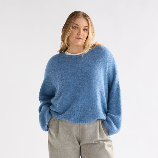 Person wearing a blue sweater and gray wide-leg pants on a white background